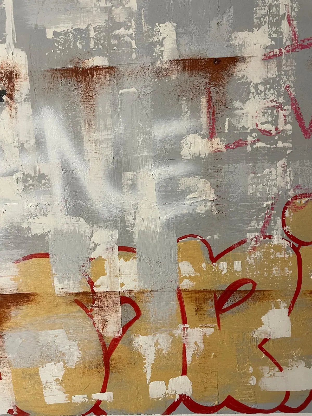 Detail of the wall's right side: a white spray-painted tag and a red outlined throw-up on yellow, both scrubbed back under layers of grey.