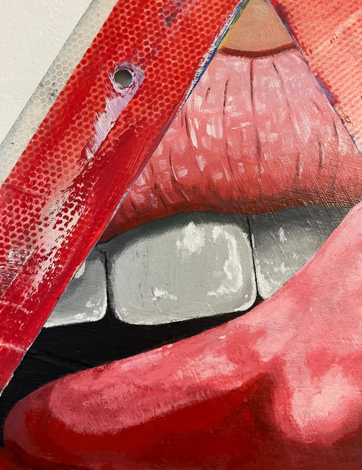 Close view of the cut-out sign: the painted mouth set into the triangular opening, with the reflective red border and a screw hole visible at the top corner.