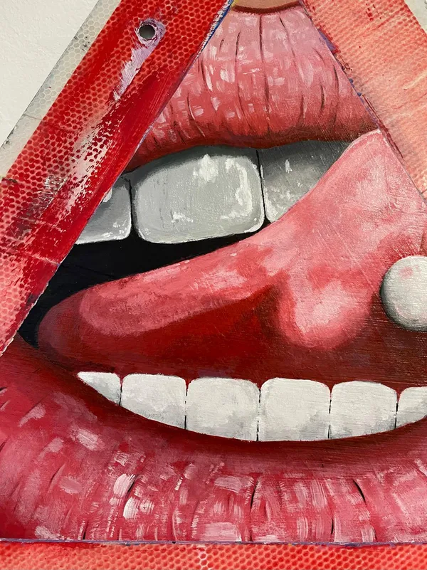 Detail of the mouth: a pink tongue pushed out over the lower teeth with a white pill resting on it, framed by the sign's cut edge.