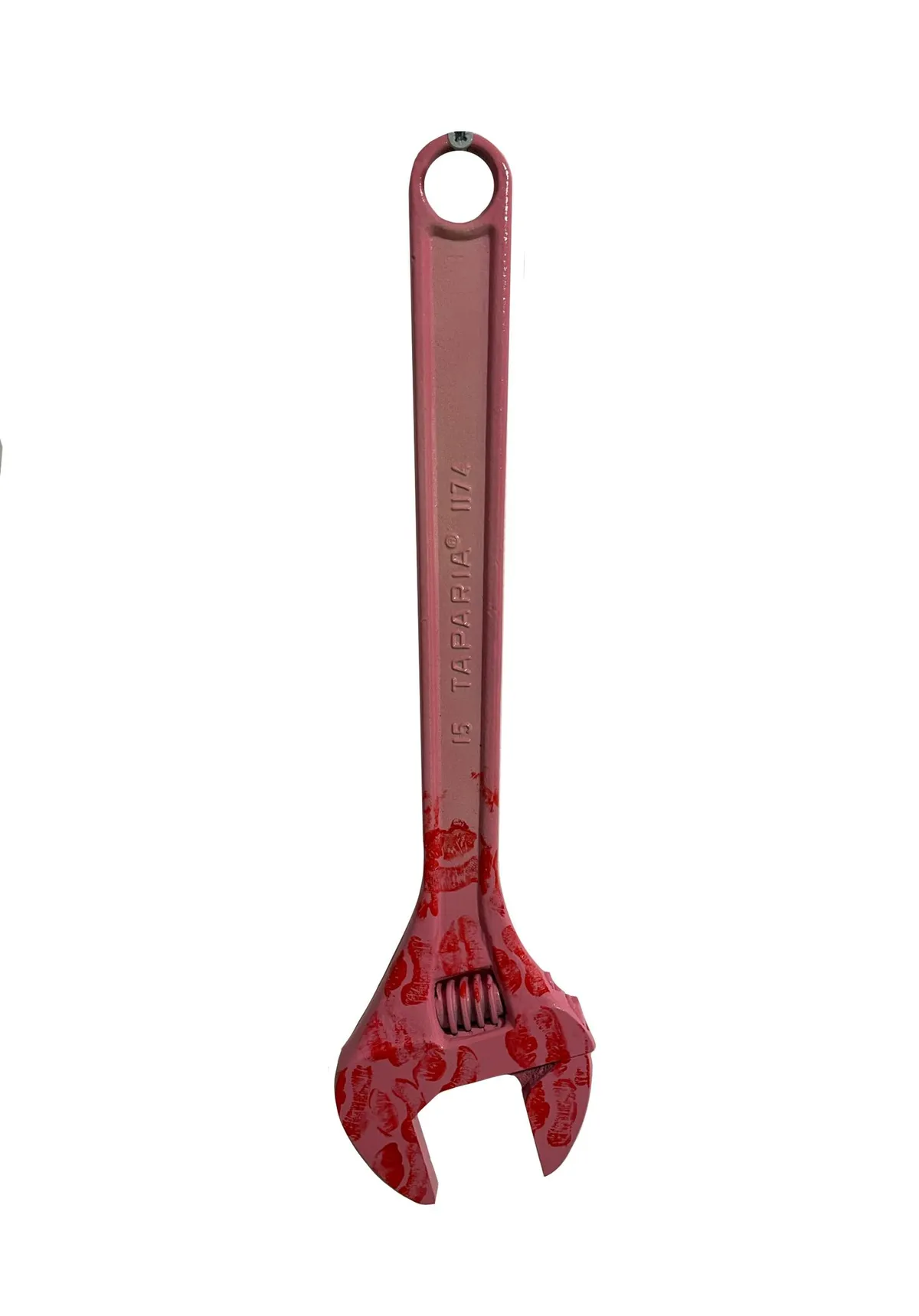 An adjustable wrench painted pink and hung by its eye, with red lipstick kiss prints crowded across the jaw and lower shaft. The Taparia maker's stamp shows through the paint.