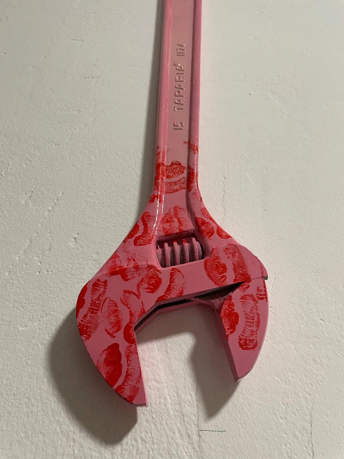 The wrench seen from the hanging eye down to the jaw, the maker's stamp legible through the pink paint and the kiss prints thinning out up the shaft.