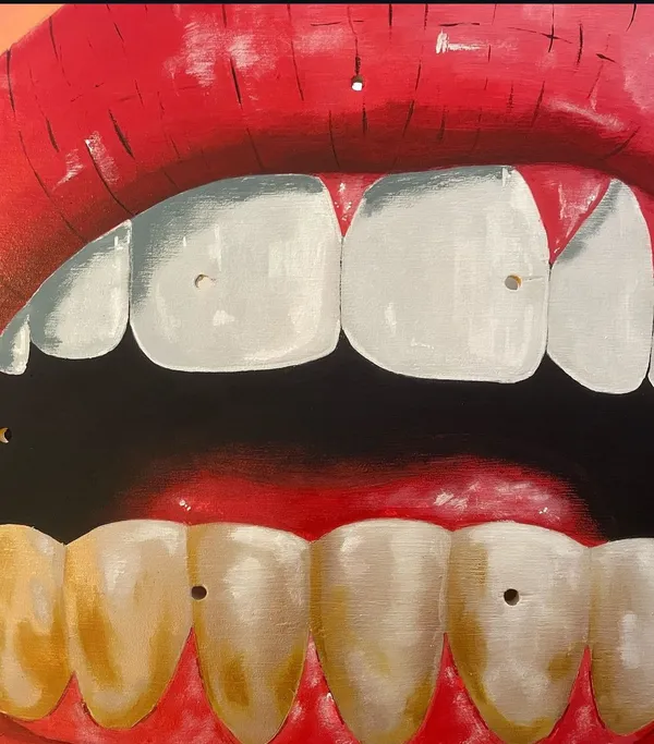 Close view of the painted blade: red lips with white upper teeth and yellowed lower teeth against a black interior, the blade's own mounting holes showing as small dots through the paint.